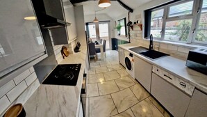 Une cuisine moderne équipée d’une cuisinière, d’un évier et d’un lave-linge, donnant sur un coin repas avec vue sur l’extérieur.