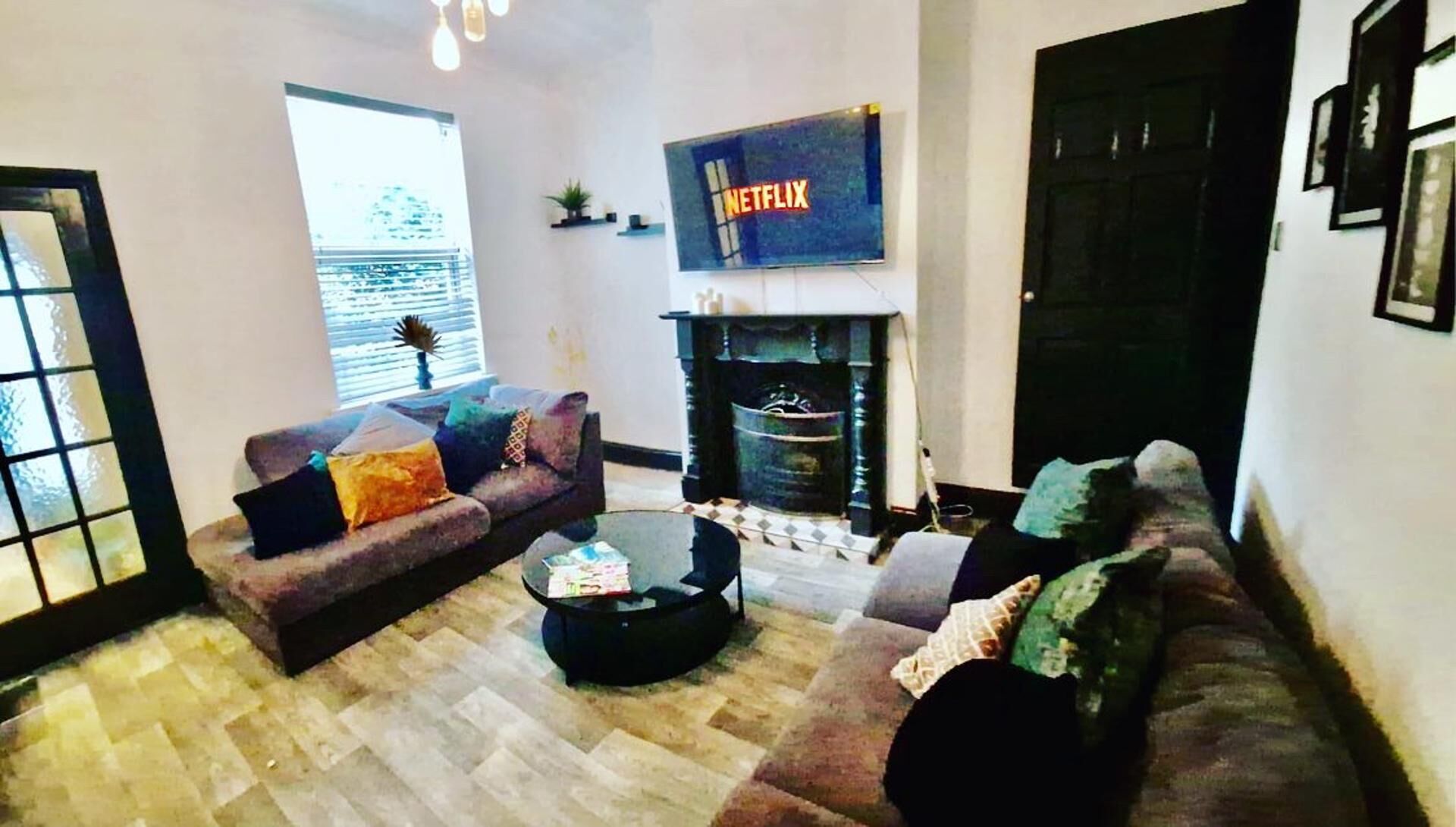 A living room with a sofa set, a coffee table, a fireplace, and a large TV screen displaying the Netflix logo.