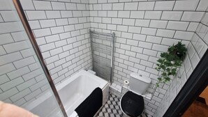 Une salle de bain avec des murs carrelés de blanc, une baignoire blanche, des toilettes et un espace douche.