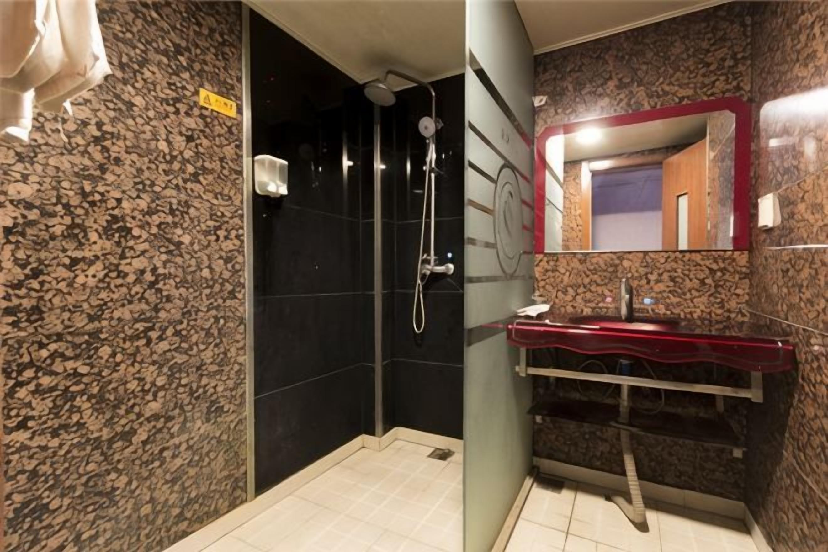 Ein Badezimmer mit Dusche, Waschbecken mit roter Ablage und Spiegel mit rotem Rahmen.