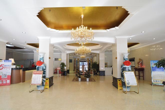 Un vestíbulo de hotel con una araña, mostrador de recepción y carteles informativos.