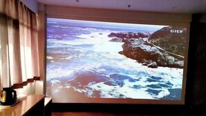 A projection of a coastal landscape with rocky cliffs and waves, a wooden table with a coffee maker, and a GIVV sign on the wall. - Zhongyuan Dasha Business Hotel (Zhengzhou)
