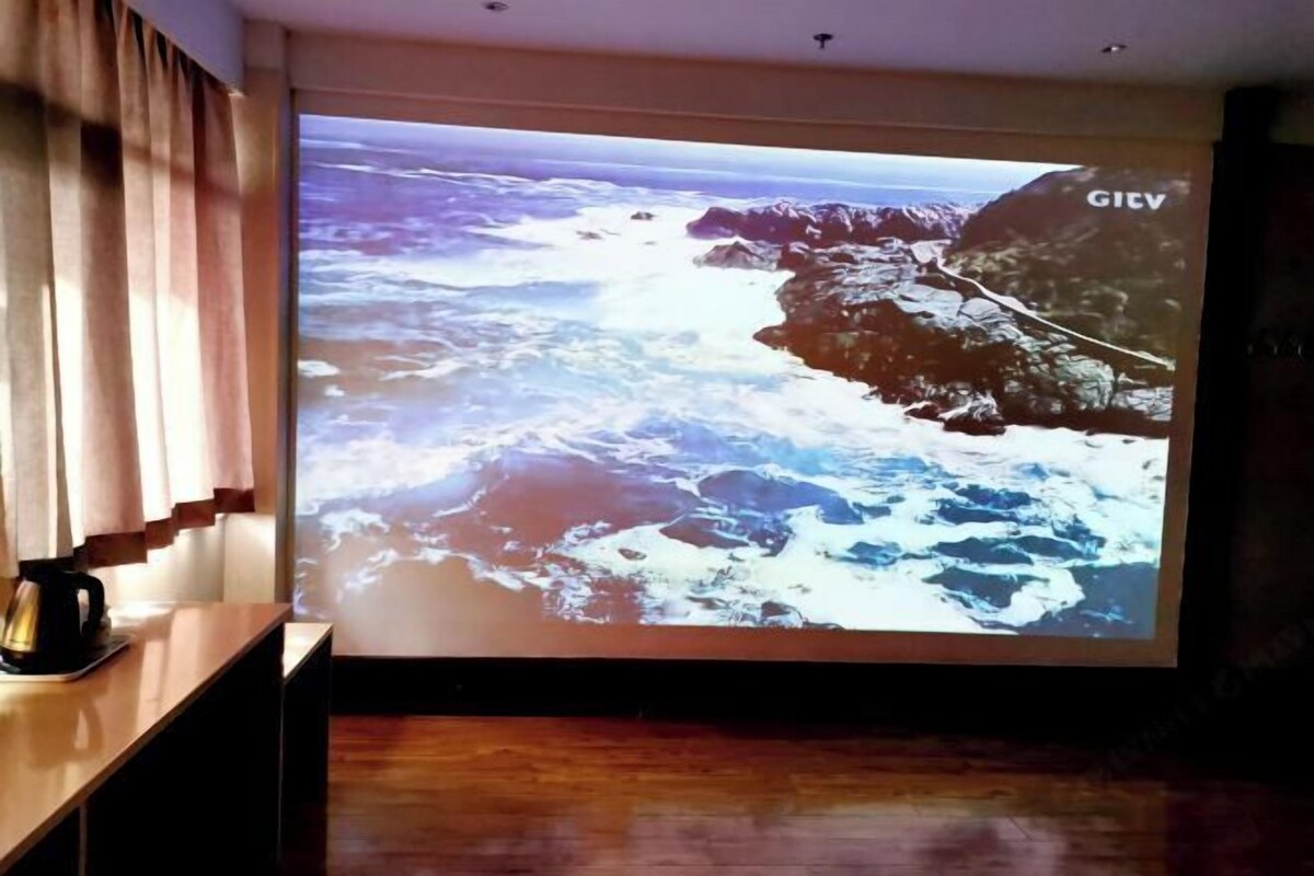 Une projection représentant un paysage côtier avec des falaises rocheuses et des vagues, une table en bois avec une machine à café, et un panneau GIVV sur le mur.