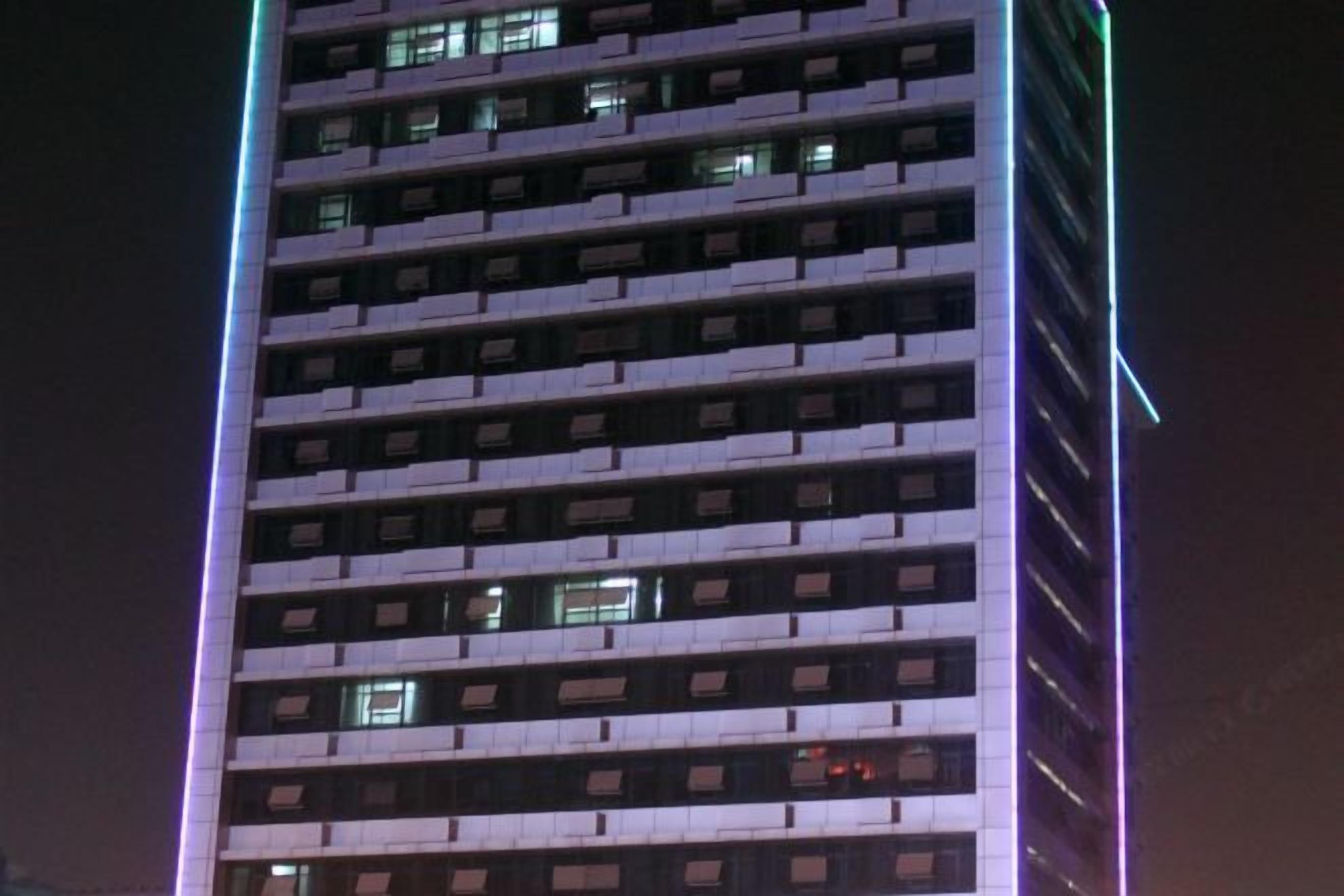 Ein hohes, mehrgeschossiges Gebäude mit modernem architektonischem Design, das eine Reihe gleichmäßig verteilter Fenster und eine auffällige vertikale Lichtleiste an der Fassade aufweist.