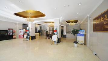 A spacious lobby with a reception desk, chandeliers, and informational posters.