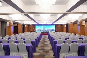 A conference room with rows of tables and chairs, a stage with a large screen, and a carpeted floor. - Zhongyuan Dasha Business Hotel (Zhengzhou)