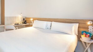Una habitación de hotel con una cama grande, una mesita de noche con lámpara, un escritorio pequeño y una silla.