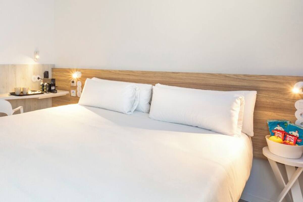 Una habitación de hotel con una cama grande, una mesita de noche con lámpara, un escritorio pequeño y una silla.
