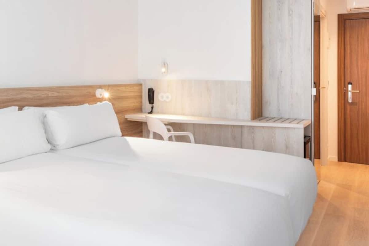 Una habitación de hotel moderna con una cama grande, una mesita de noche y un escritorio con una silla.