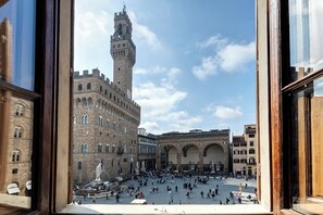 Una plaza histórica con una torre destacada y estatuas, rodeada de edificios tradicionales.