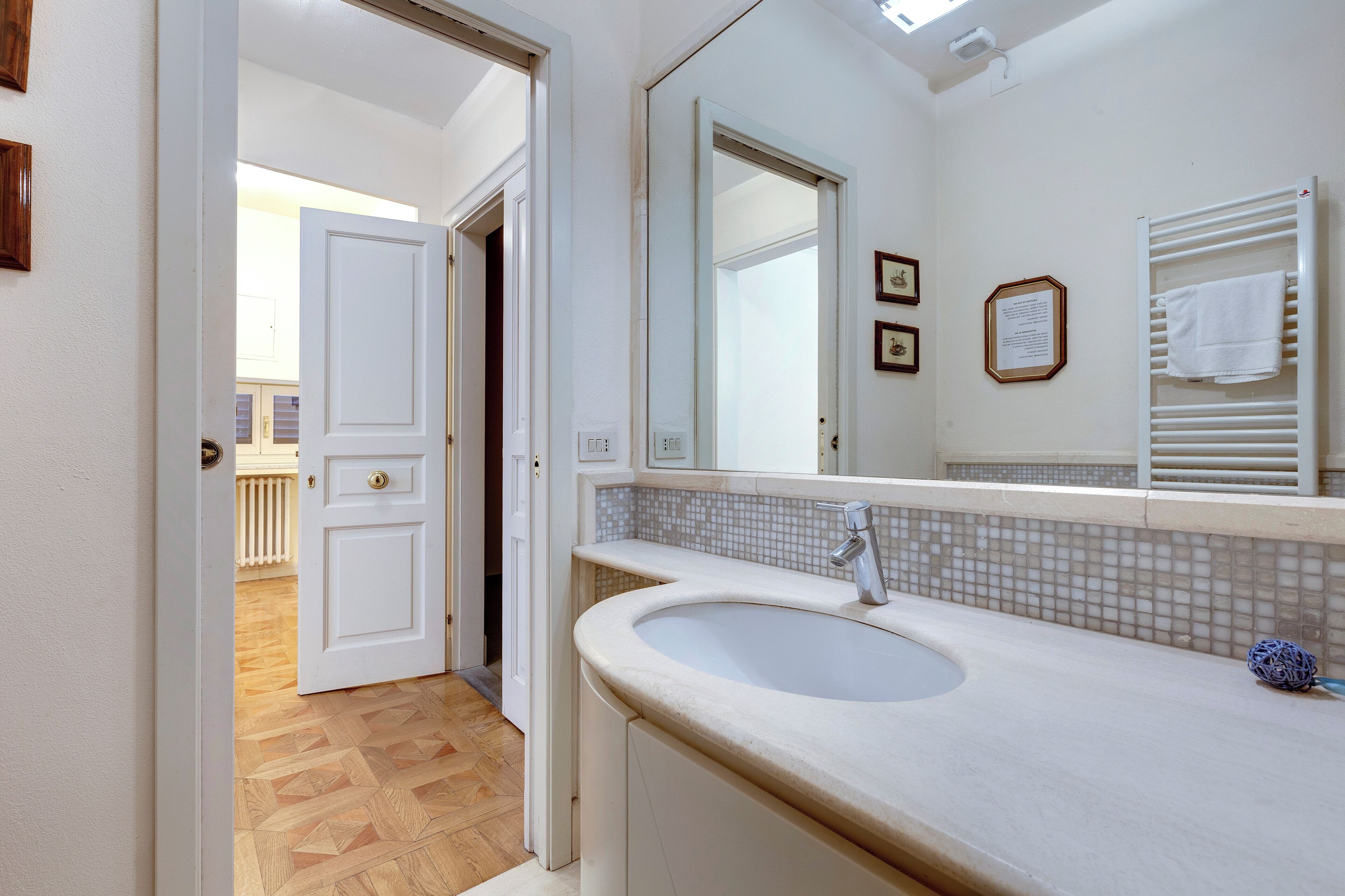 Un baño con lavamanos blanco, un espejo y un perchero para toallas.