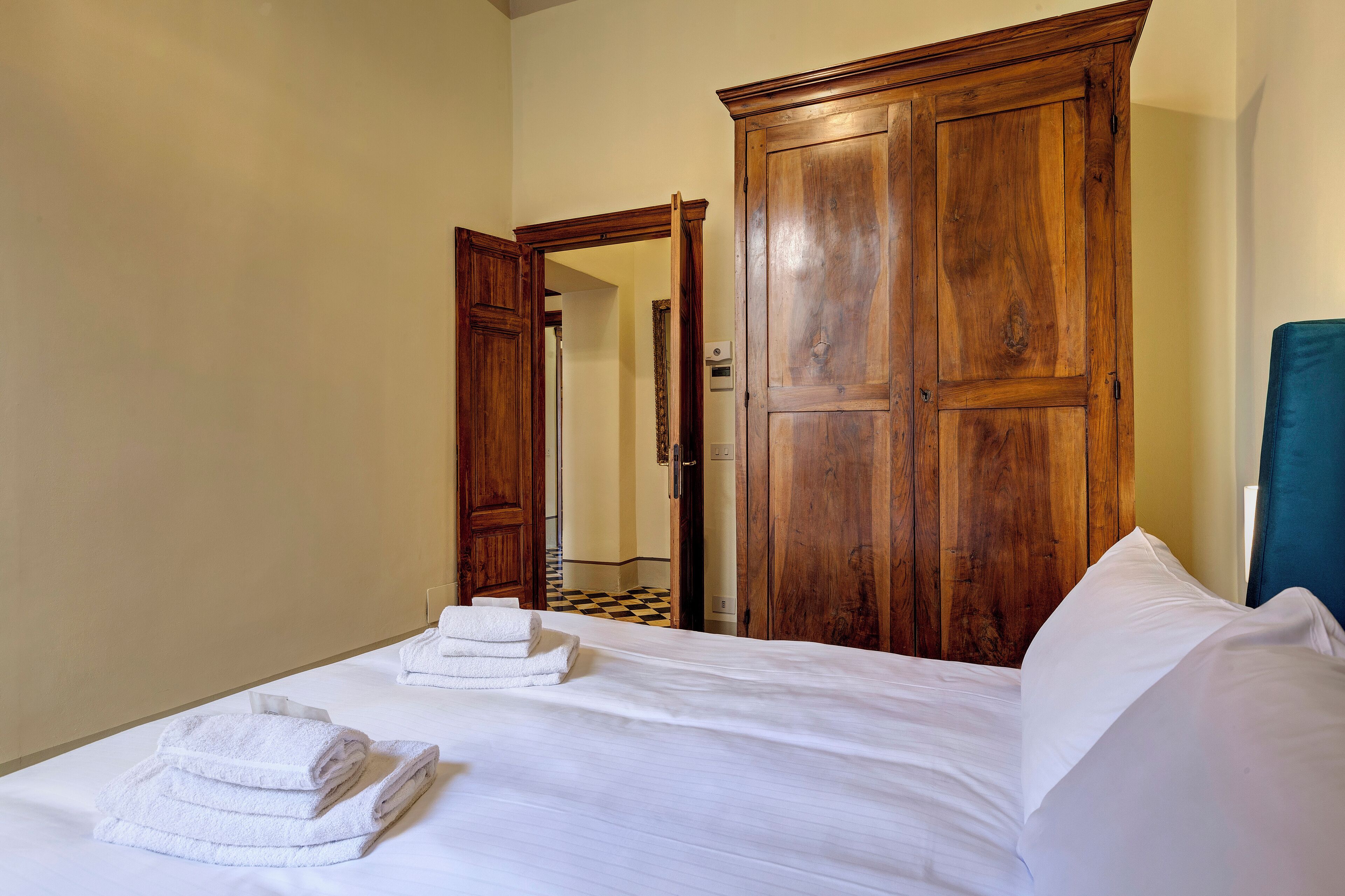 Una habitación de hotel con un amplio armario de madera, una cama con ropa blanca y un suelo a cuadros.