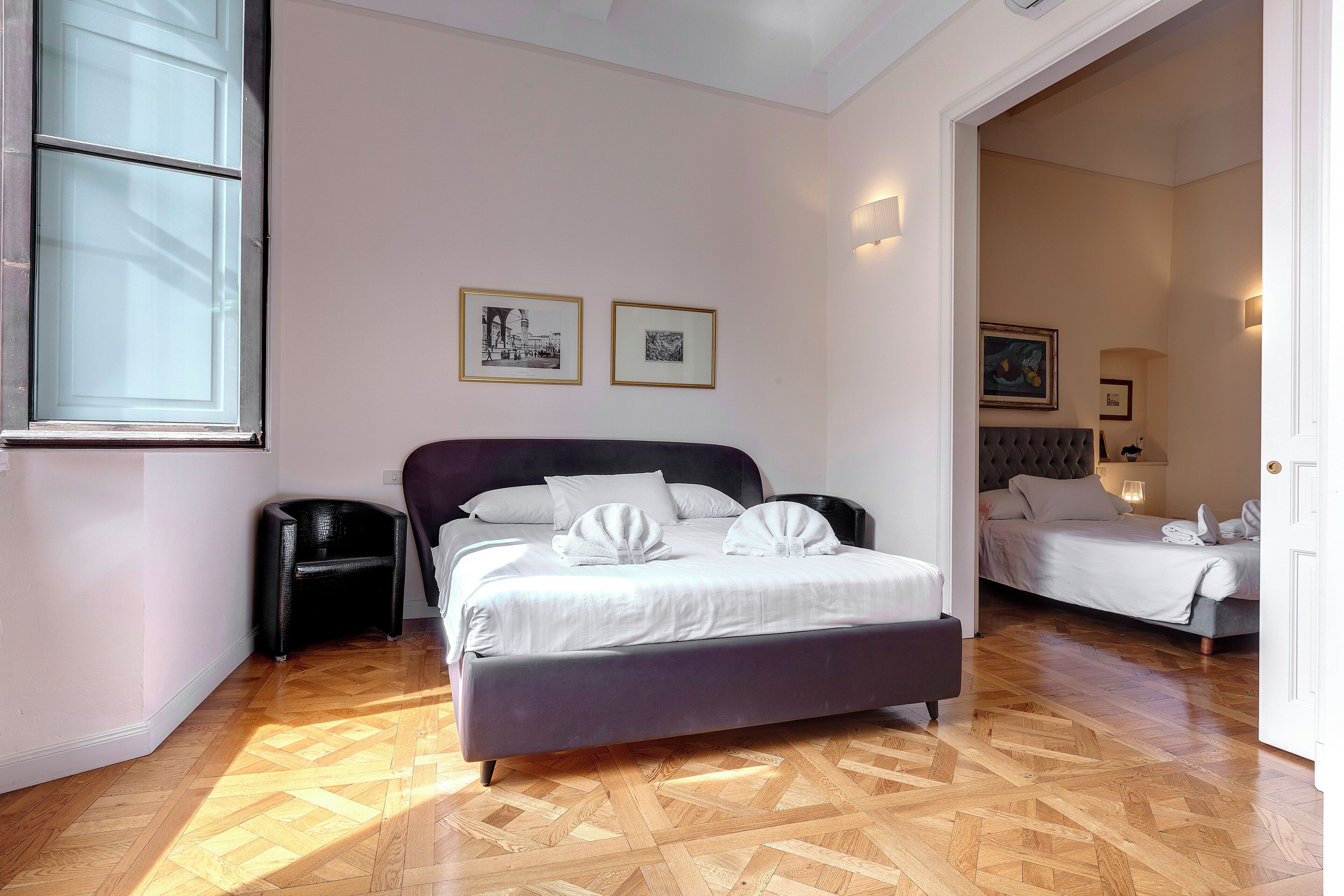 A bedroom with a large bed, a smaller bed, and a nightstand. There are two framed pictures on the wall.