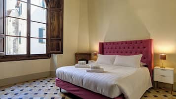 A bedroom with a large bed, a wooden wardrobe, a nightstand with a lamp, and a window with shutters.