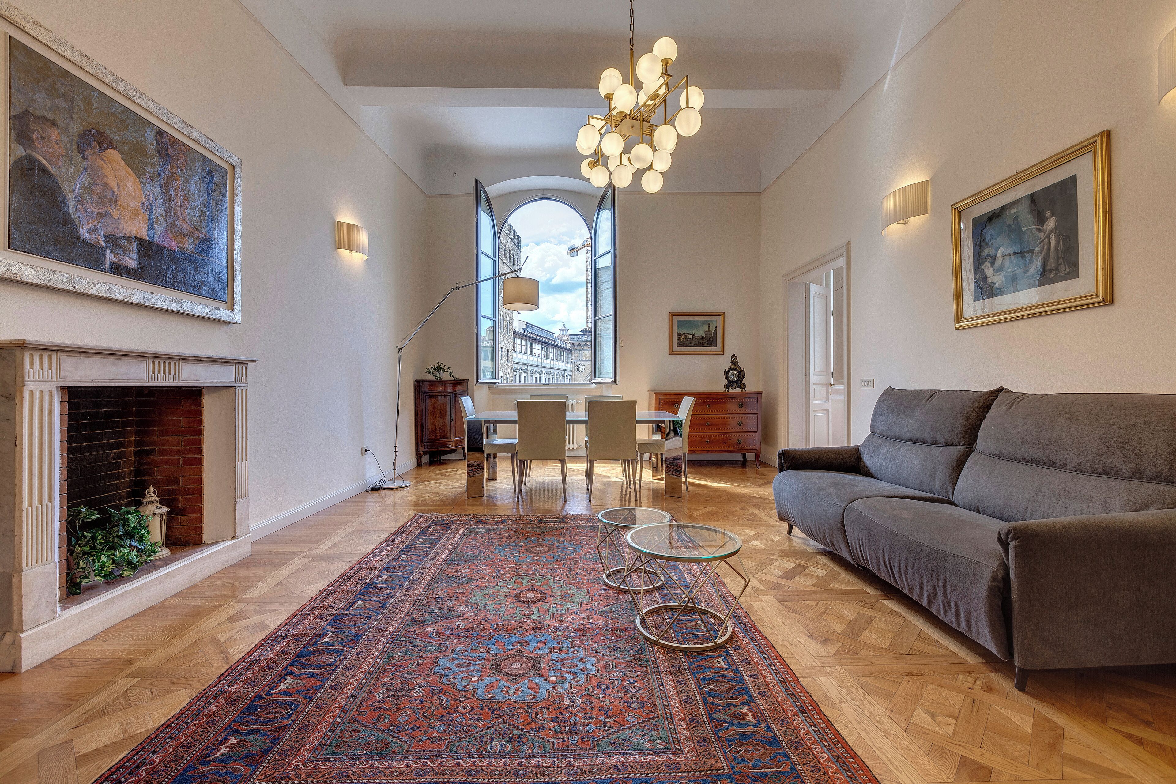 A spacious living room with a fireplace, a large rug, a sofa, and a dining area with chairs and a table.