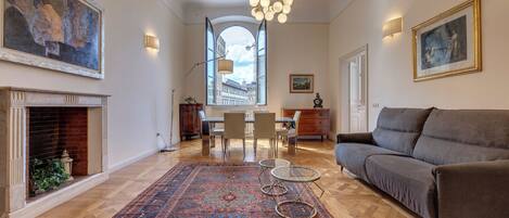 A spacious living room with a fireplace, a large rug, a sofa, and a dining area with chairs and a table.