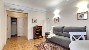 A living room with a grey sofa, a patterned rug, a white chair, and a wooden cabinet.