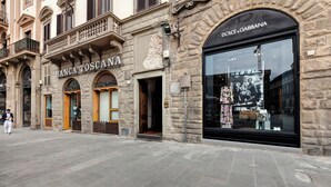 Vista de una calle con comercios, incluyendo 'BANCA TOSCANA' y 'DOLCE & GABBANA'.