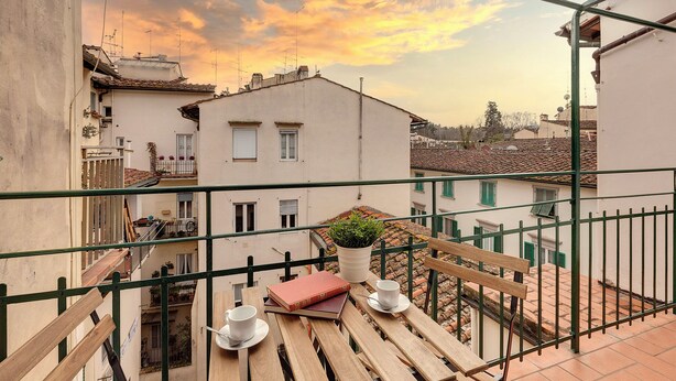 A balcony with a wooden table, two cups, and a book. - Mamo Florence - Maddalena Apartment (Florence)