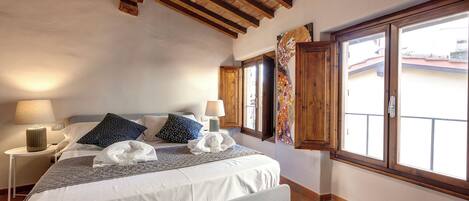 A bedroom with a large bed, wooden beams, a window with a view, and a nightstand with a lamp.