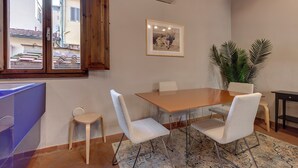 A dining area with a wooden table, white chairs, a small side table, and a potted plant. - Mamo Florence - Magazzini Apartment (Florence)