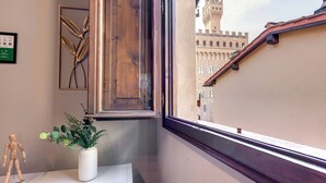 A corner of a room with a wooden window frame, a white vase with green foliage, and a wooden mannequin. A framed picture hangs on the wall. - Mamo Florence - Magazzini Apartment (Florence)