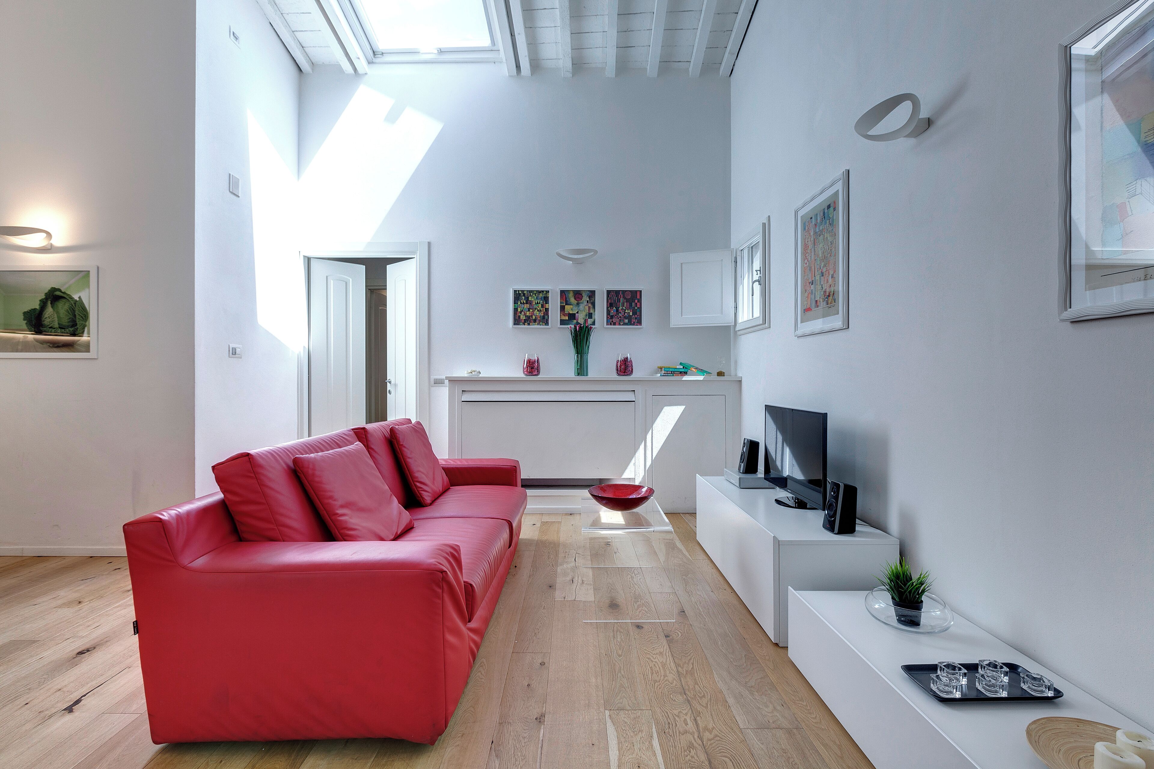 A modern living room with a red sofa, a TV, and a kitchen area in the background.
