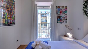 A bedroom with a bed, a nightstand, a lamp, and a view of the outside balcony. - Mamo Florence - Margot Apartment (Florence)