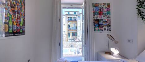 Une chambre à coucher avec un lit, une table de chevet, une lampe et une vue sur le balcon extérieur.