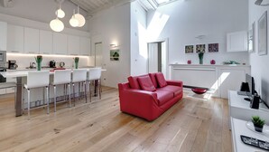 A modern kitchen with white cabinets, a dining area with white chairs, a red leather sofa, and a skylight. - Mamo Florence - Margot Apartment (Florence)
