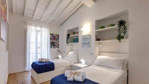A hotel room with two beds, a large window with curtains, a wall-mounted shelf with decorative items, and a framed sign on the wall. - Mamo Florence - Margot Apartment (Florence)