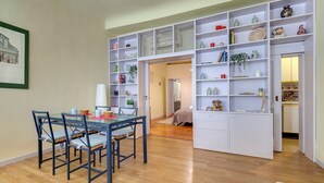 Ein moderner Wohnraum mit Essbereich, integrierten Regalen und Dekorationselementen sowie einem sichtbaren Schlafzimmer.