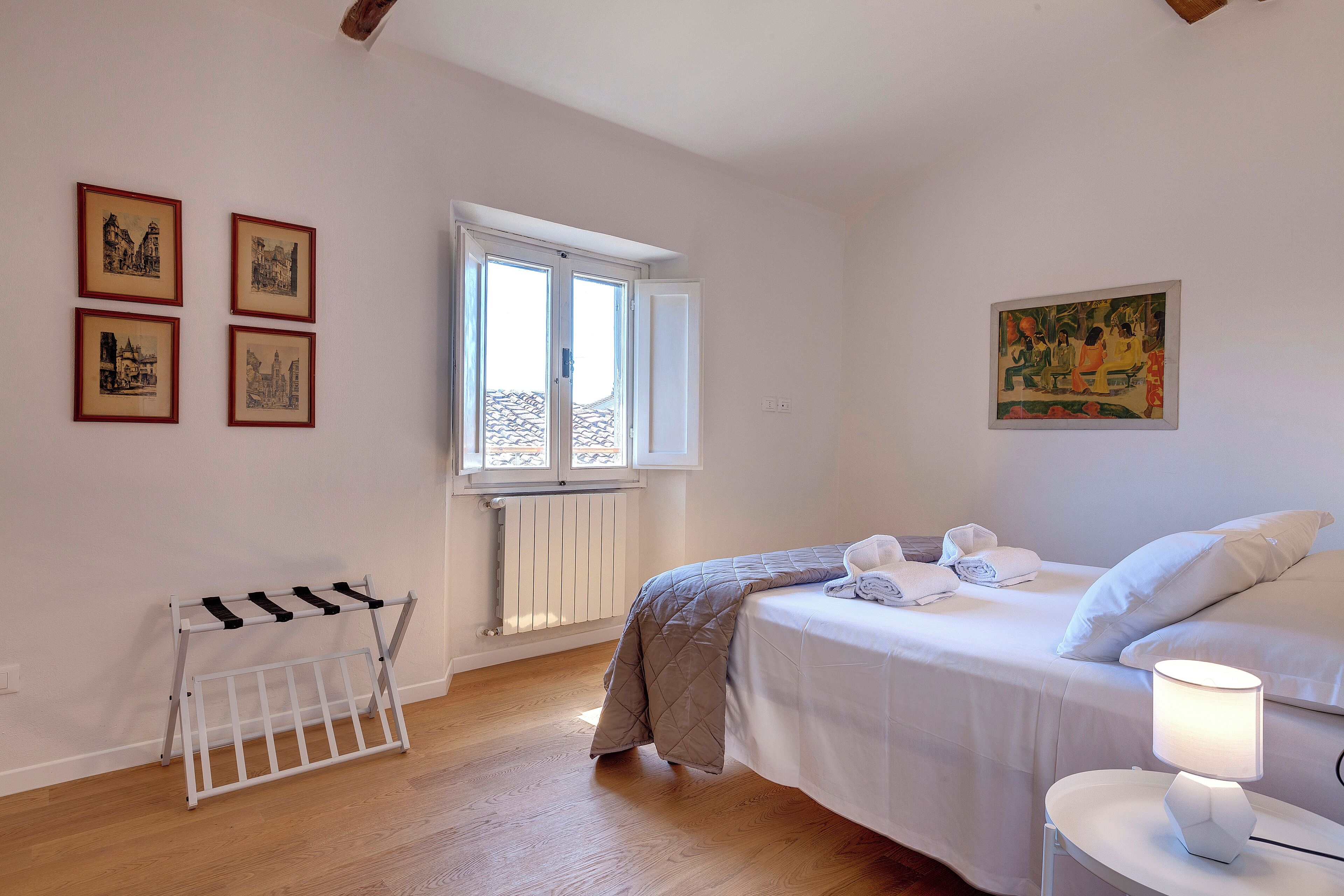 Un dormitorio con cama, mesita de noche con lámpara, radiador y ventana.