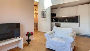 A modern living room with a flat-screen TV, a white sofa, and a vase with red flowers. - Mamo Florence - Pinti Apartment (Florence)