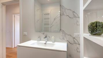 Un baño moderno con lavamanos de mármol blanco, un espejo grande y una planta verde en un estante.