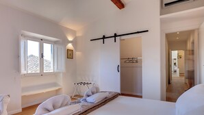 A bedroom with a bed, a window, a drying rack, and a hallway leading to another room. - Mamo Florence - Pinti Apartment (Florence)