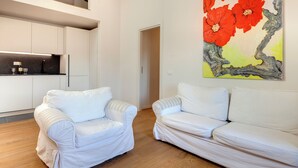 A modern living room with two white sofas, a kitchen with white cabinets, and a large painting of red flowers on the wall. - Mamo Florence - Pinti Apartment (Florence)