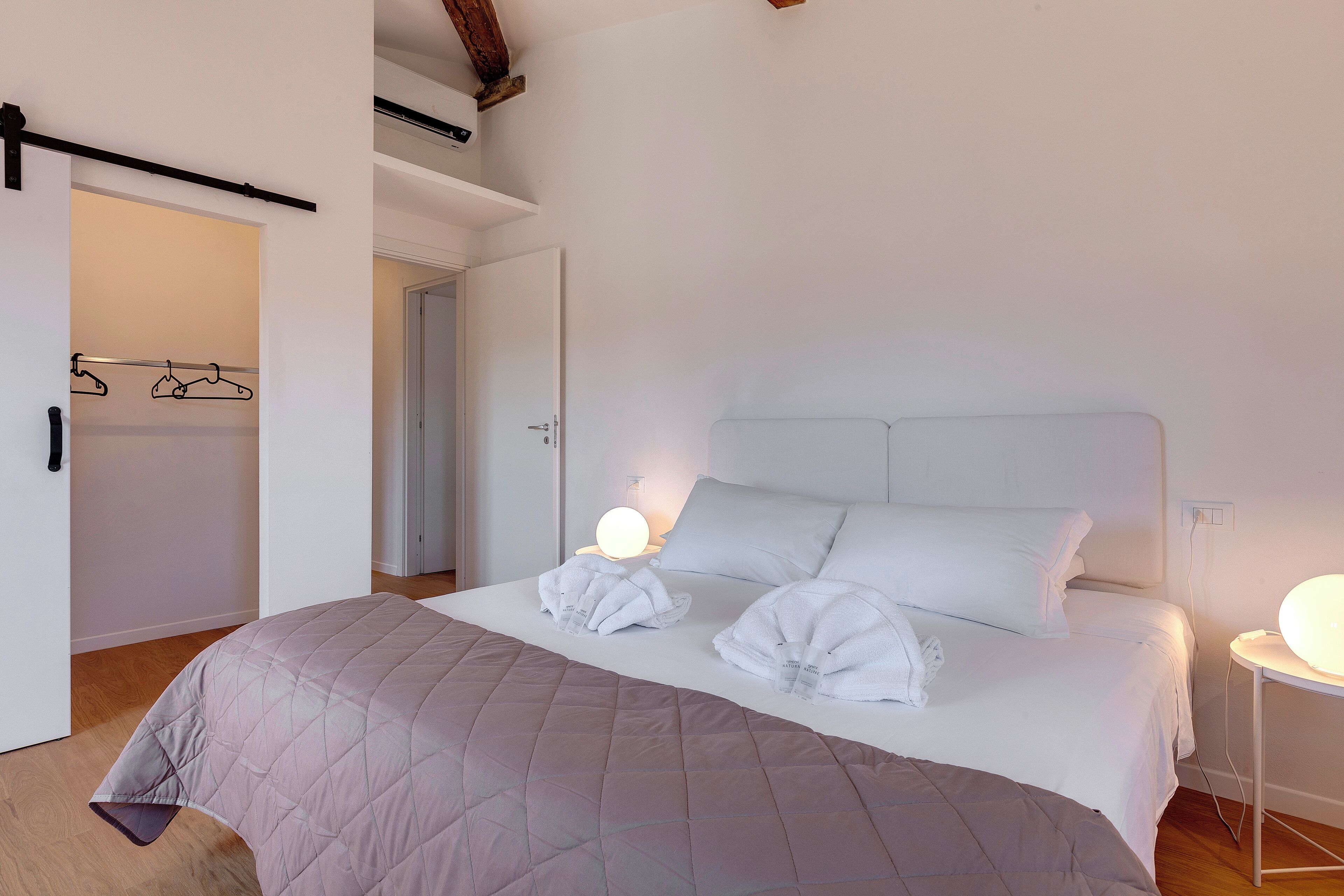 Cama bem arrumada com cobertura acolchoada, duas luminárias de cabeceira e mesa de cabeceira com abajur.