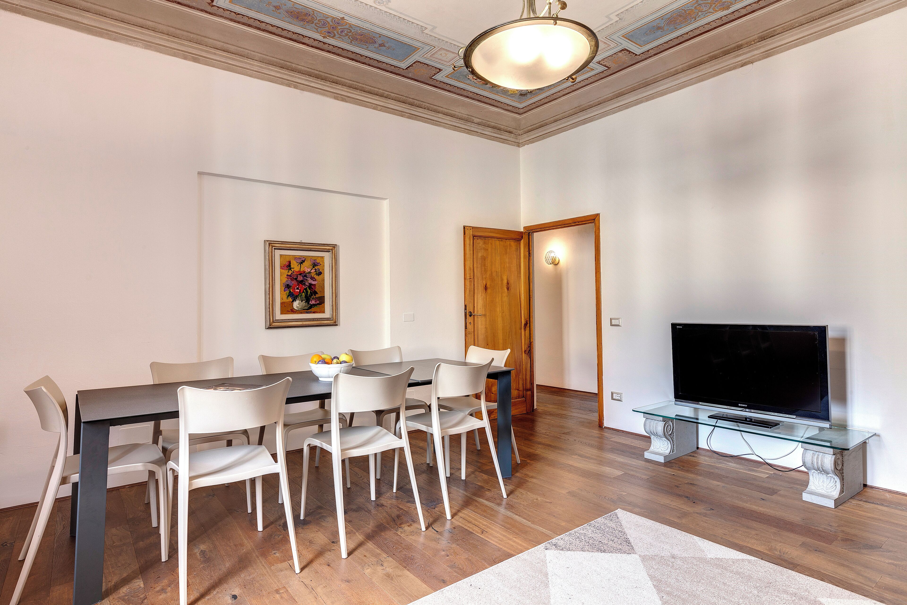 Een eetgedeelte met een rechthoekige tafel, zes stoelen, een glazen salontafel en een flatscreen televisie op een standaard.