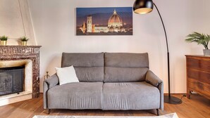 A living room with a grey sofa, a fireplace, a floor lamp, and a painting of a cityscape.