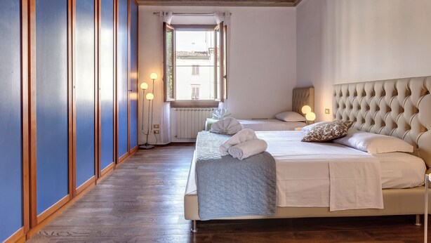 A hotel room with a large bed, a view through an open window, and a wooden floor.