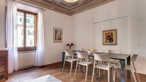 A dining area with a table and chairs, a window with curtains, and a radiator.