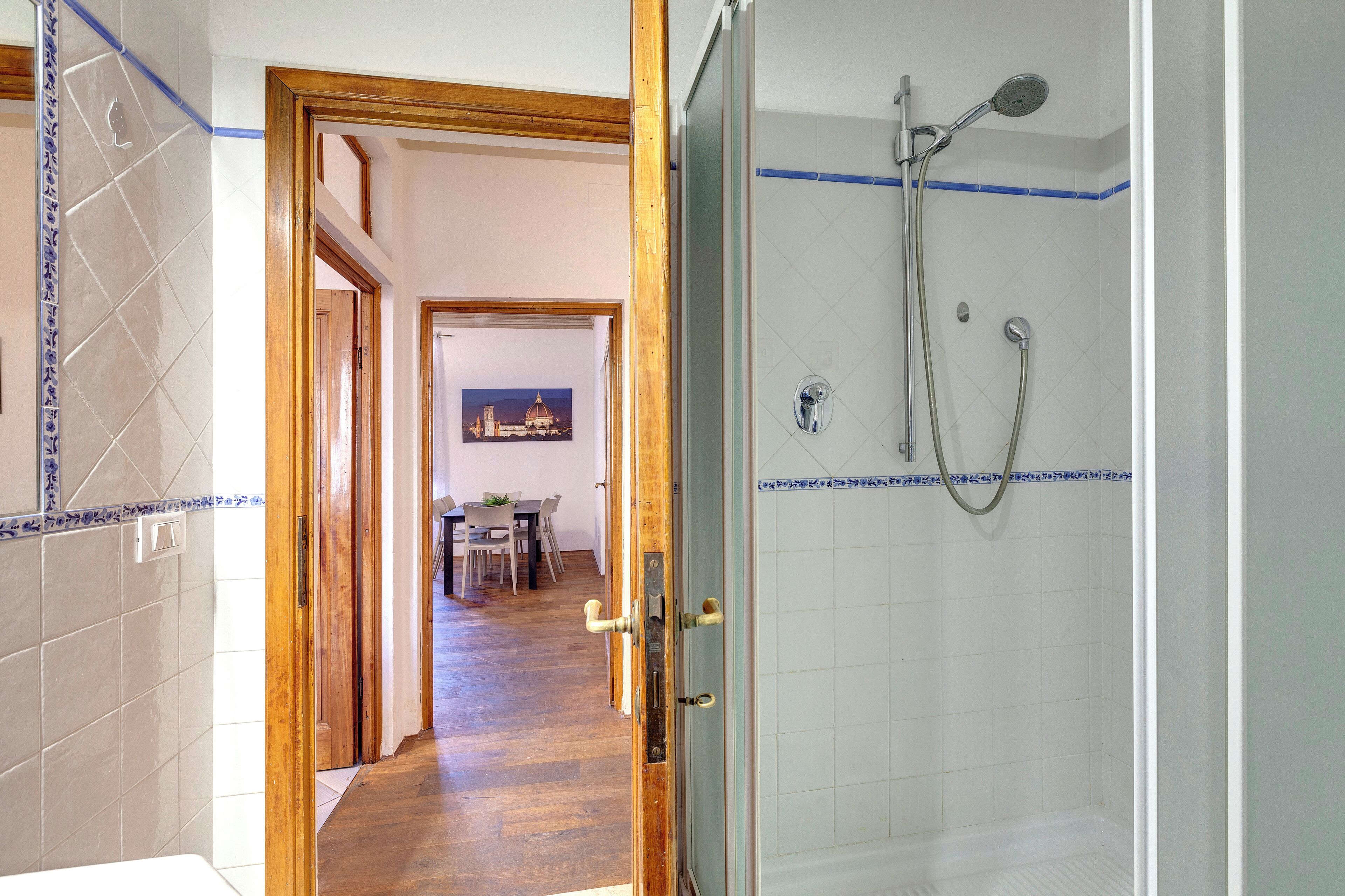 A bathroom with a shower, tiled walls, and a wooden door leading to a dining area.