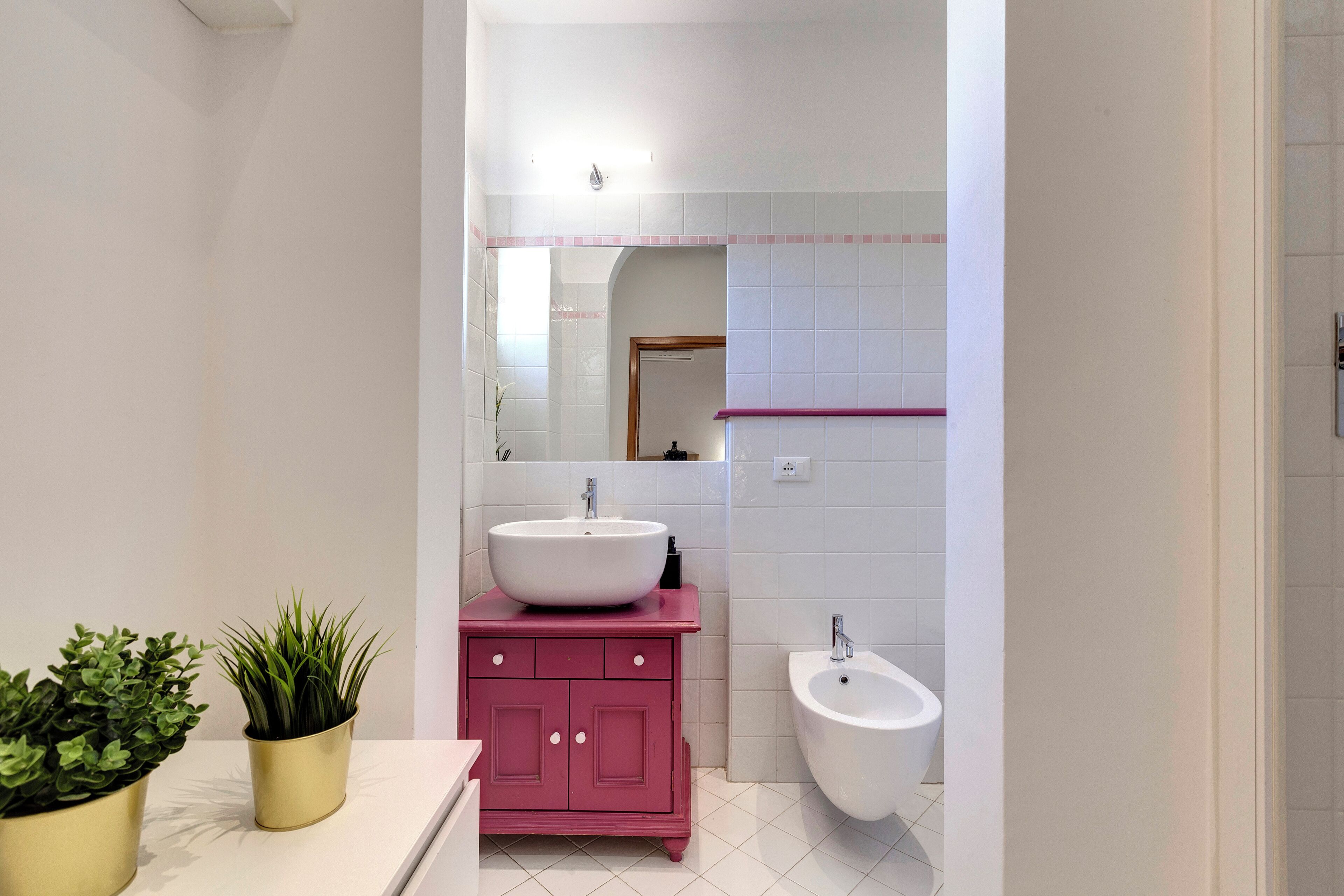 A modern bathroom with a white sink, pink vanity, and a bidet.