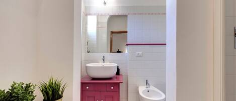 A modern bathroom with a white sink, pink vanity, and a bidet.