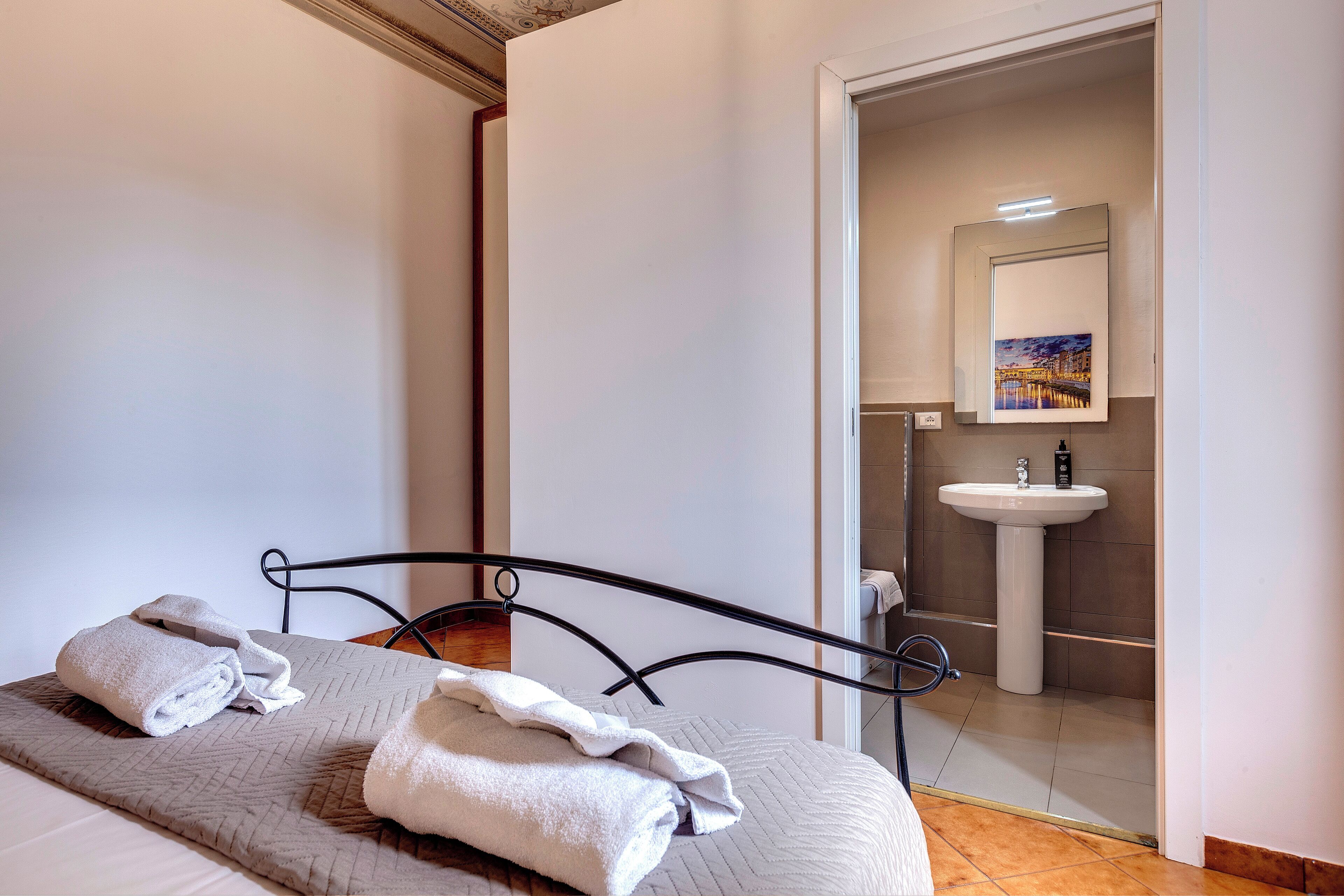 A hotel room with a bed, towels, a bathroom with a sink and mirror, and a painting on the wall.