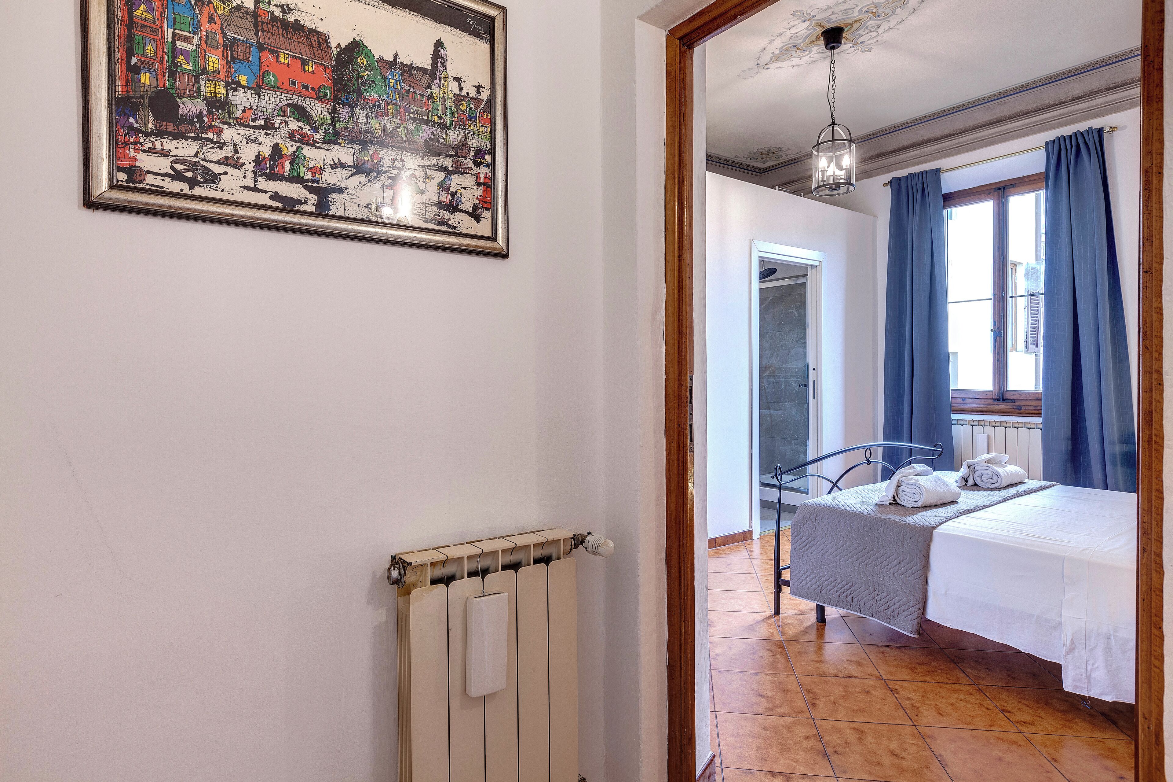 A room with a bed, a radiator, a framed picture, and a window with curtains.