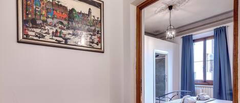 A room with a bed, a radiator, a framed picture, and a window with curtains.