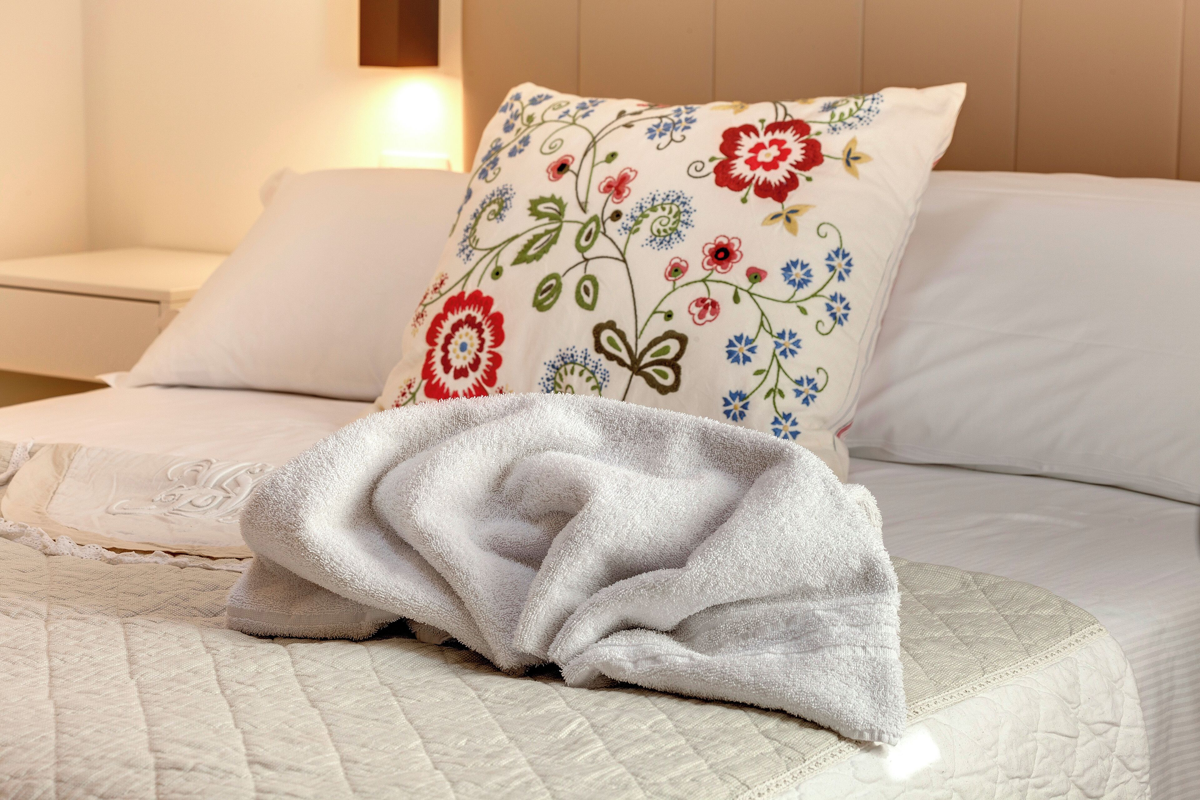 A neatly made bed with a quilted bedspread and a decorative pillow with floral embroidery.