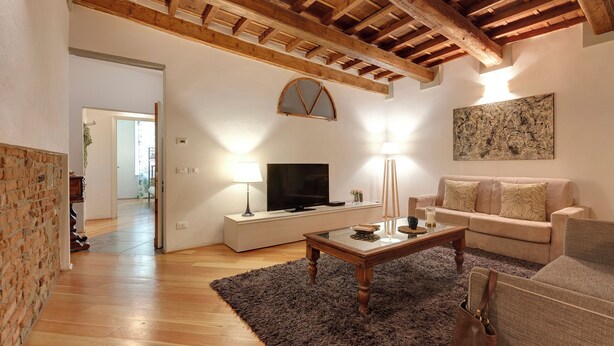 A living room with a wooden ceiling, a television, a sofa, and a coffee table. - Mamo Florence - San Lorenzo Apartment (Florence)